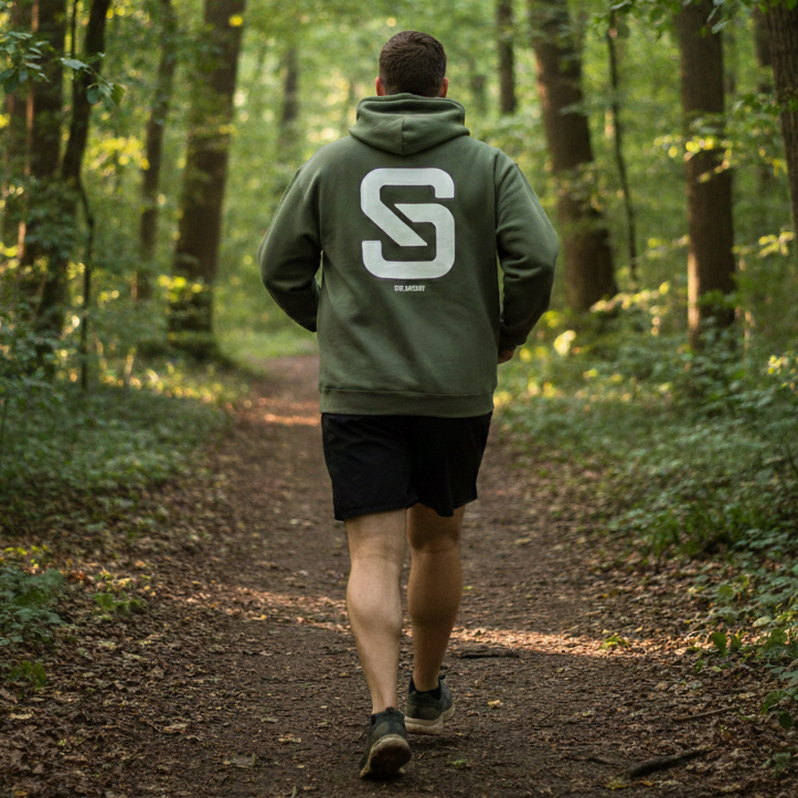 Person walking through a forest wearing a green hoodie with a logo.
